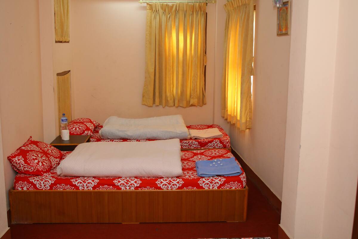 A single bed with red and white bedding, a wooden headboard, and a small bedside table with a bottle and a tissue box.