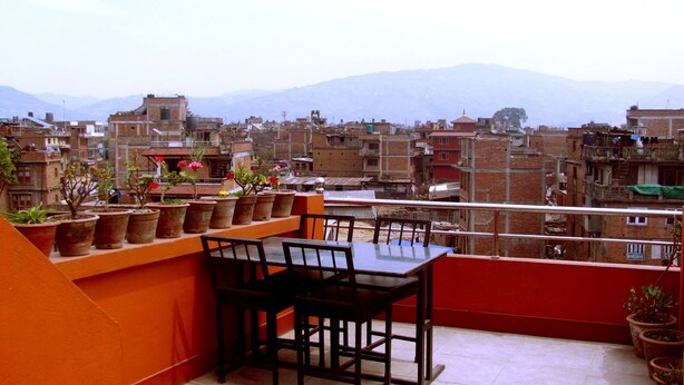 A balcony with a table and chairs, potted plants, and a view of a cityscape with mountains in the background. - Swastik Guest House (Bhaktapur)