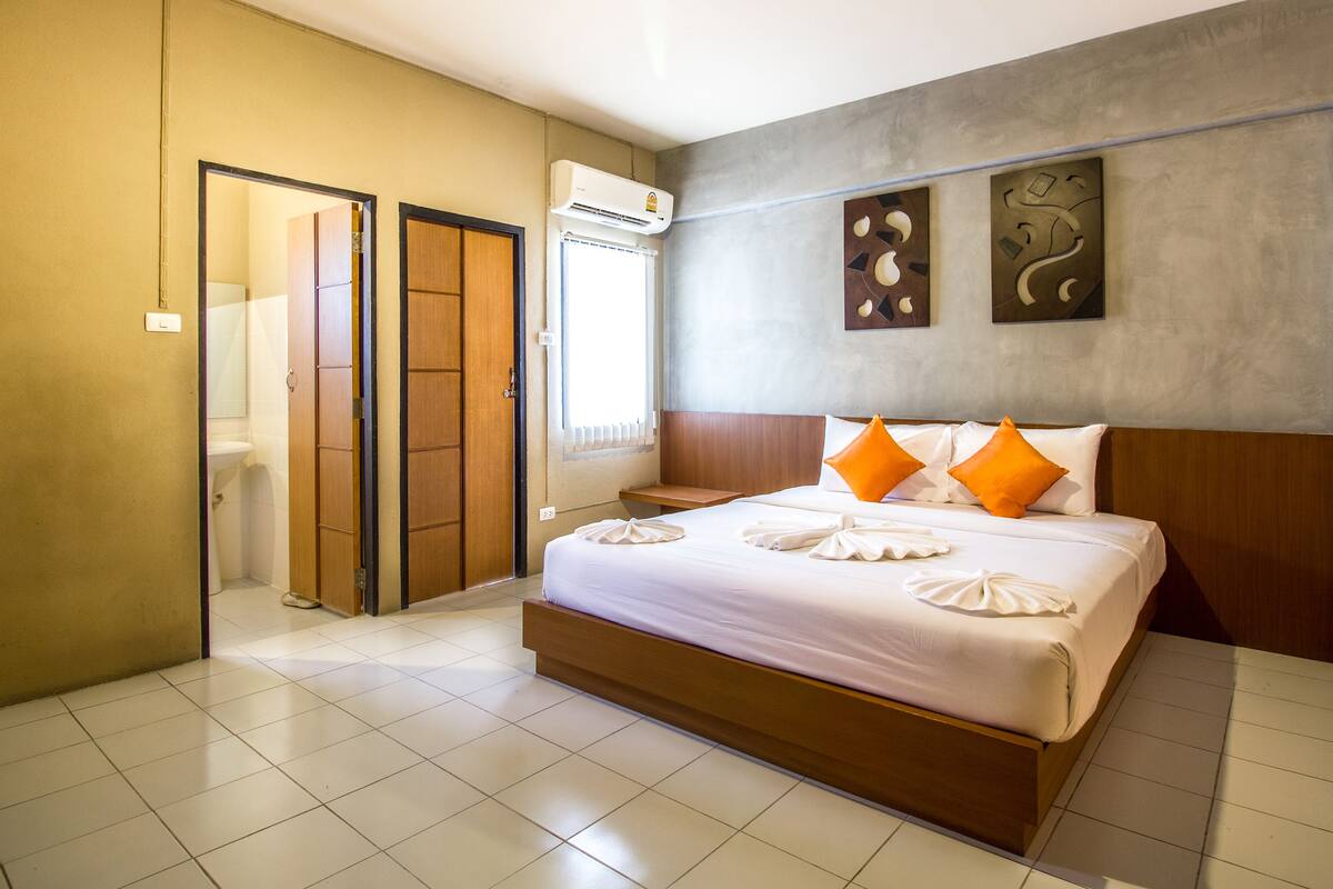 A hotel room with a large bed, a wooden headboard, and a wall-mounted air conditioner.