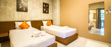 A hotel room with two beds, wooden headboards, white bedding, orange pillows, a large mirror, and a view of the bathroom.