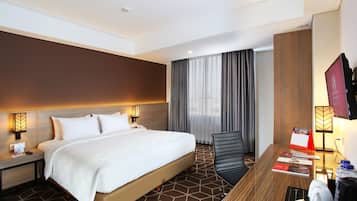 Ein Hotelzimmer mit einem großen Bett, einem Schreibtisch mit Stuhl, einem Fernseher und einem Fenster mit Vorhängen.