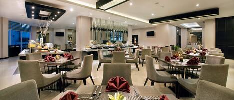 A modern dining area with multiple tables and chairs, a central buffet, and a contemporary ceiling design.