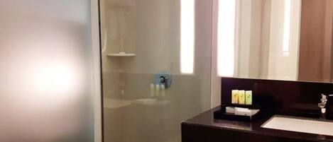 A modern bathroom with a glass shower enclosure, a dark countertop sink, and a mirror above it.