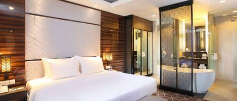 A modern hotel room with a large bed, bedside tables, a glass-enclosed bathroom, and a patterned floor.
