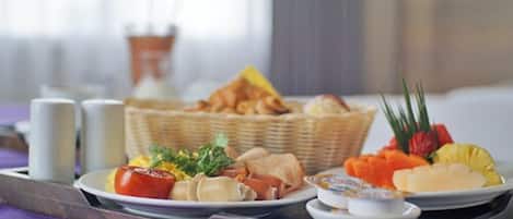 A breakfast buffet with various dishes, including fruits, pastries, and a small dish of jam.