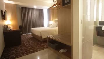 Ein Hotelzimmer mit Bett, Nachttisch, Lampe und einem Badezimmer mit Waschbecken und Spiegel.