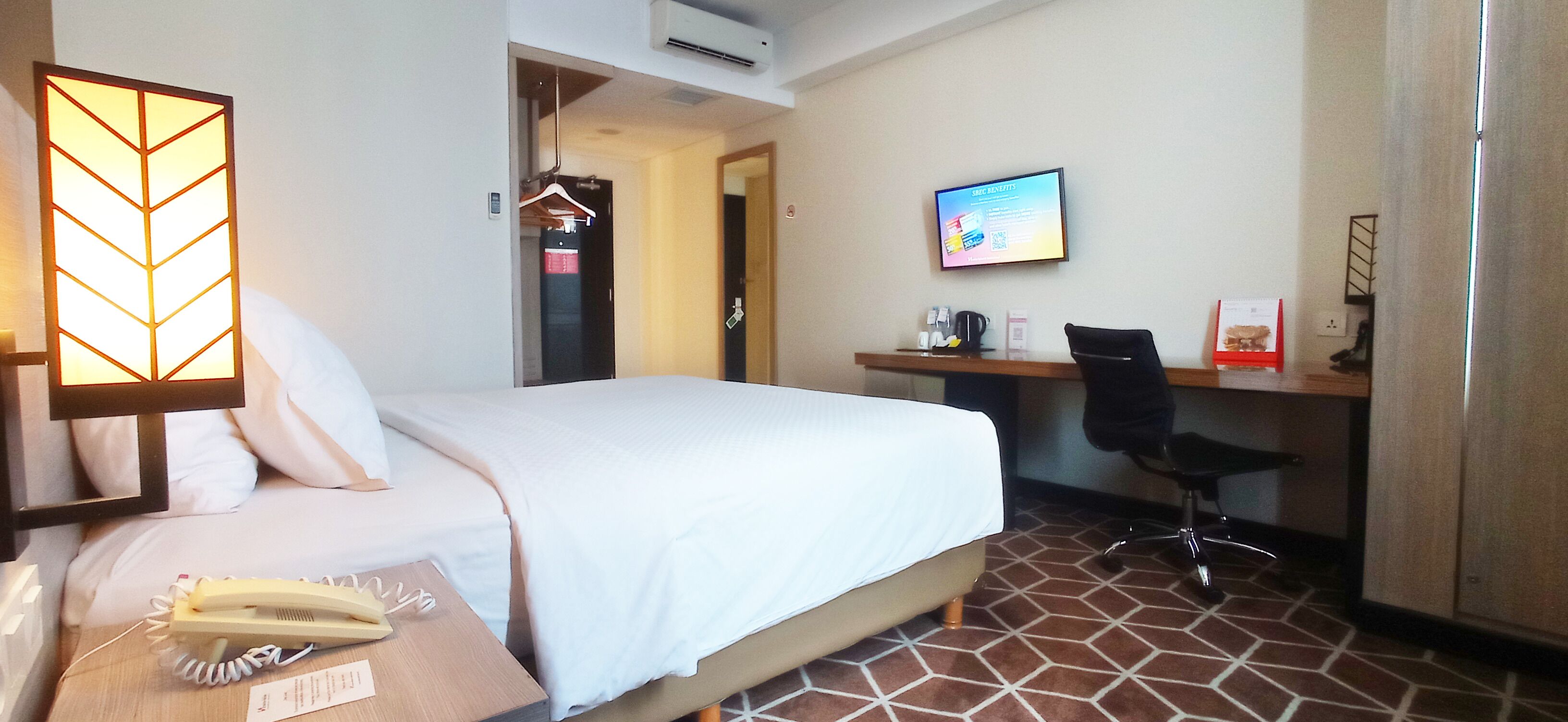 Ein Hotelzimmer mit Bett, Schreibtisch, Stuhl, Fernseher und Telefon.