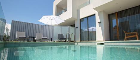 A modern pool area with clear water, lounge chairs, and a large umbrella.