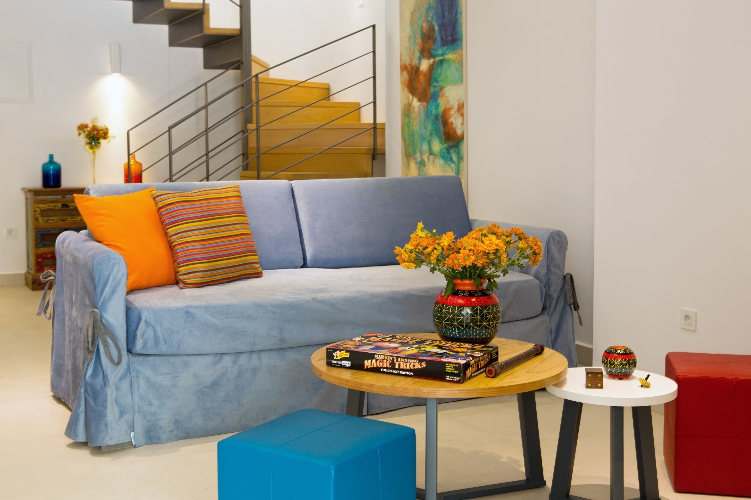 A living room with a sofa, a coffee table, and a red ottoman. There is a book titled "Marvin's Amazing Magic Tricks" on the coffee table.