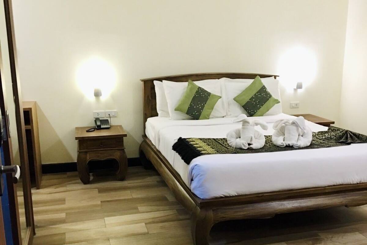 A neatly arranged hotel room with a wooden bed, a bedside table with a phone, and a wall-mounted light.