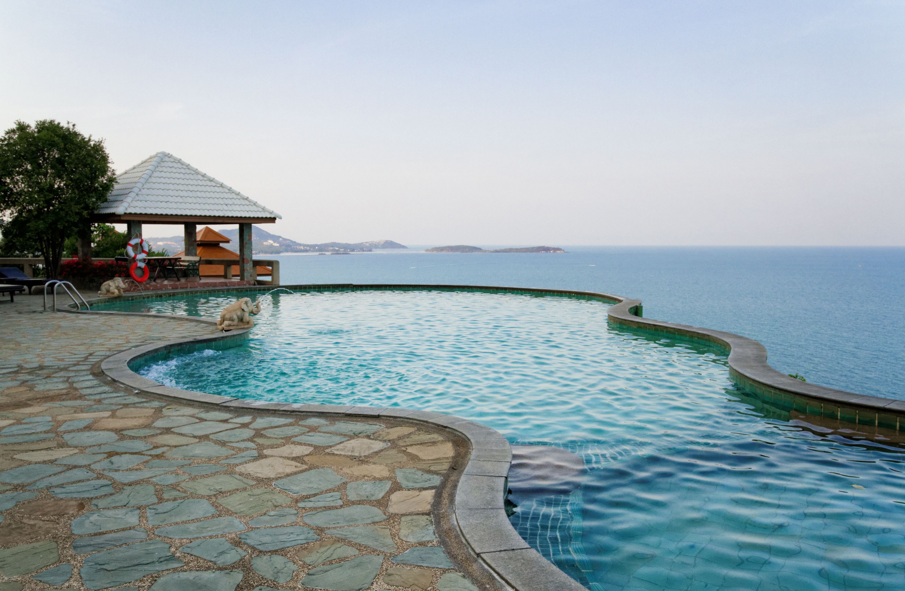 Ein Pool mit gewölbter Kante, ein Pavillon und Meerblick.