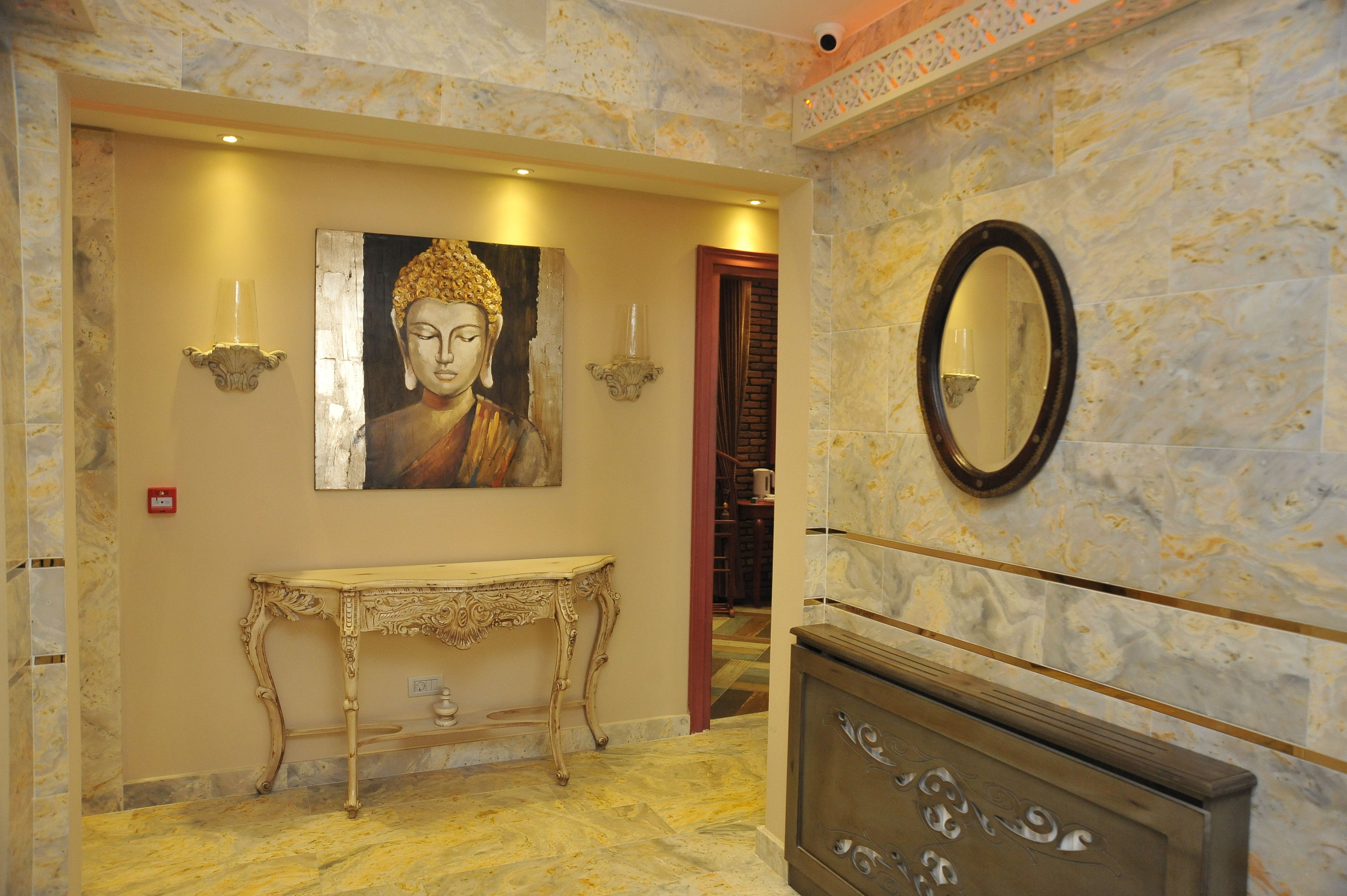 A marble-floored hallway with a Buddha painting, a console table, a wall-mounted mirror, and a red door leading to another room.