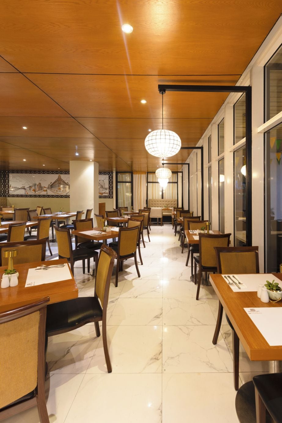 A restaurant with multiple dining tables and chairs, a chandelier, and a mural on the wall.