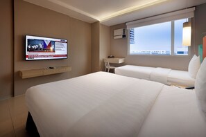Habitación de hotel con dos camas, un televisor montado en la pared, un escritorio y una ventana con vista a la ciudad.