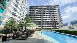 Un hotel moderno con piscina, asientos exteriores y edificios altos al fondo.
