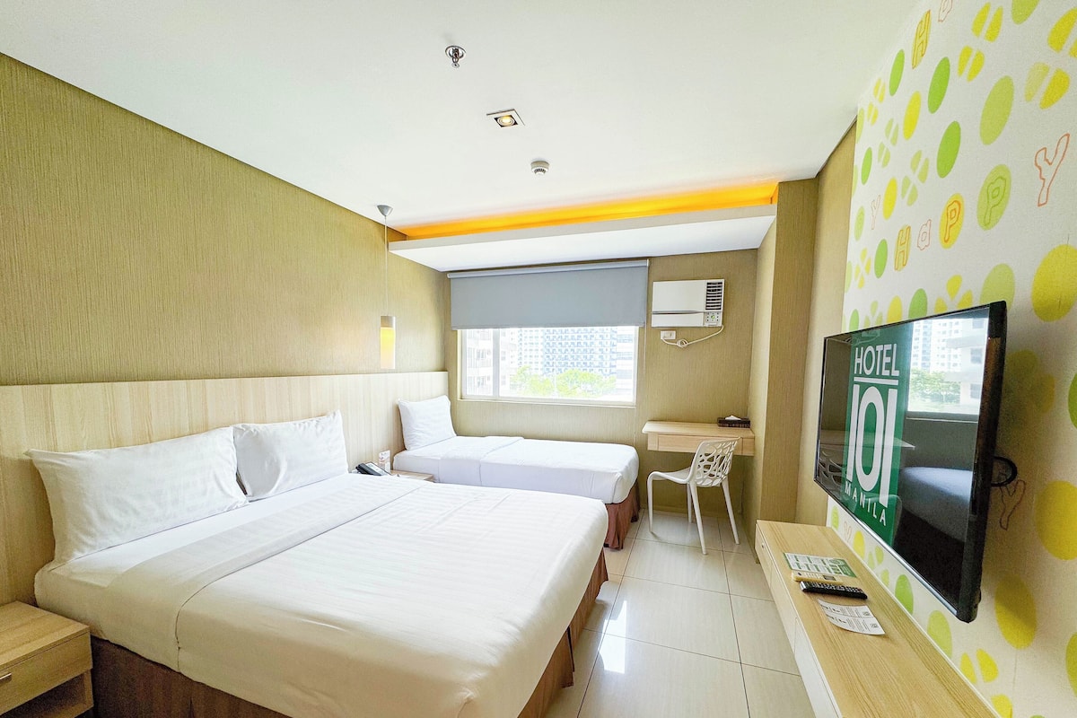 A hotel room with two beds, a desk, a chair, a TV, and a window with a city view.