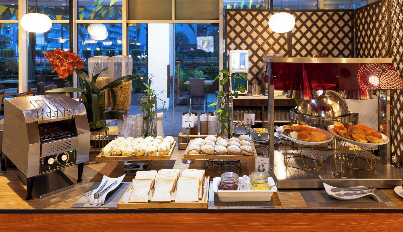 A breakfast buffet with various food items, a coffee machine, and a decorative plant.