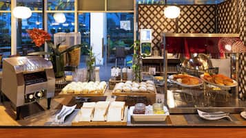A breakfast buffet with various food items, a coffee machine, and a decorative plant.