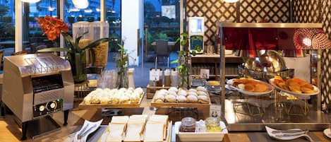 A breakfast buffet with various food items, a coffee machine, and a decorative plant.