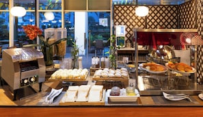 A breakfast buffet with various food items, a coffee machine, and a decorative plant.