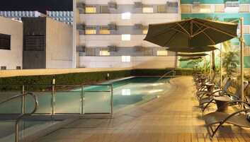 A poolside area with a glass barrier, lounge chairs, and an umbrella.