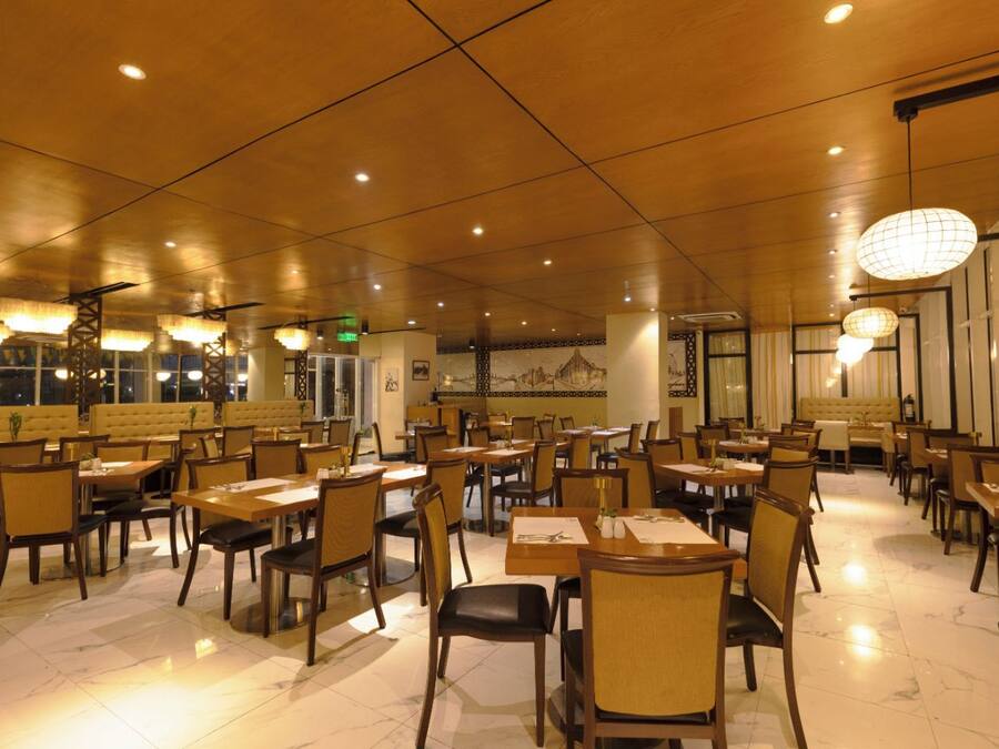 A spacious restaurant with multiple dining tables and chairs, a high ceiling with recessed lighting, and a large mural on the back wall.