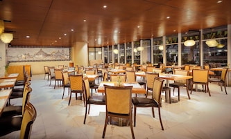 A restaurant with multiple tables and chairs, a mural on the wall, and large windows.