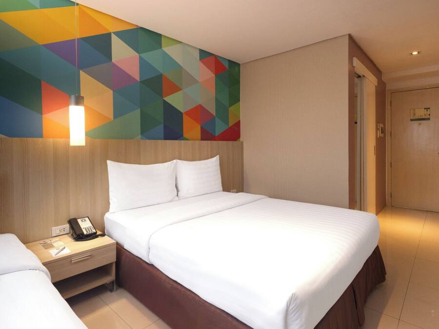 Habitación de hotel con cama, mesita de noche y un llamativo diseño geométrico en la pared.