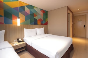 A hotel room with a bed, bedside table, and a colorful geometric wall design.