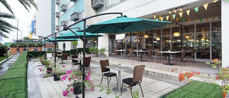 An outdoor patio area with tables and chairs, surrounded by greenery and potted plants.