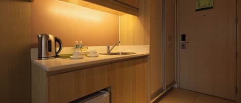 A compact kitchenette with a stainless steel kettle, a coffee maker, and a small refrigerator.