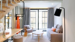 A modern living room with a sofa, a coffee table, and a chair. There is a staircase with a railing and a hanging light fixture.