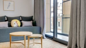 A modern living room with a grey sofa, two wooden side tables, and a large window with grey curtains.
