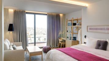 Habitación de hotel con cama, escritorio, silla, sofá y ventana con cortinas.