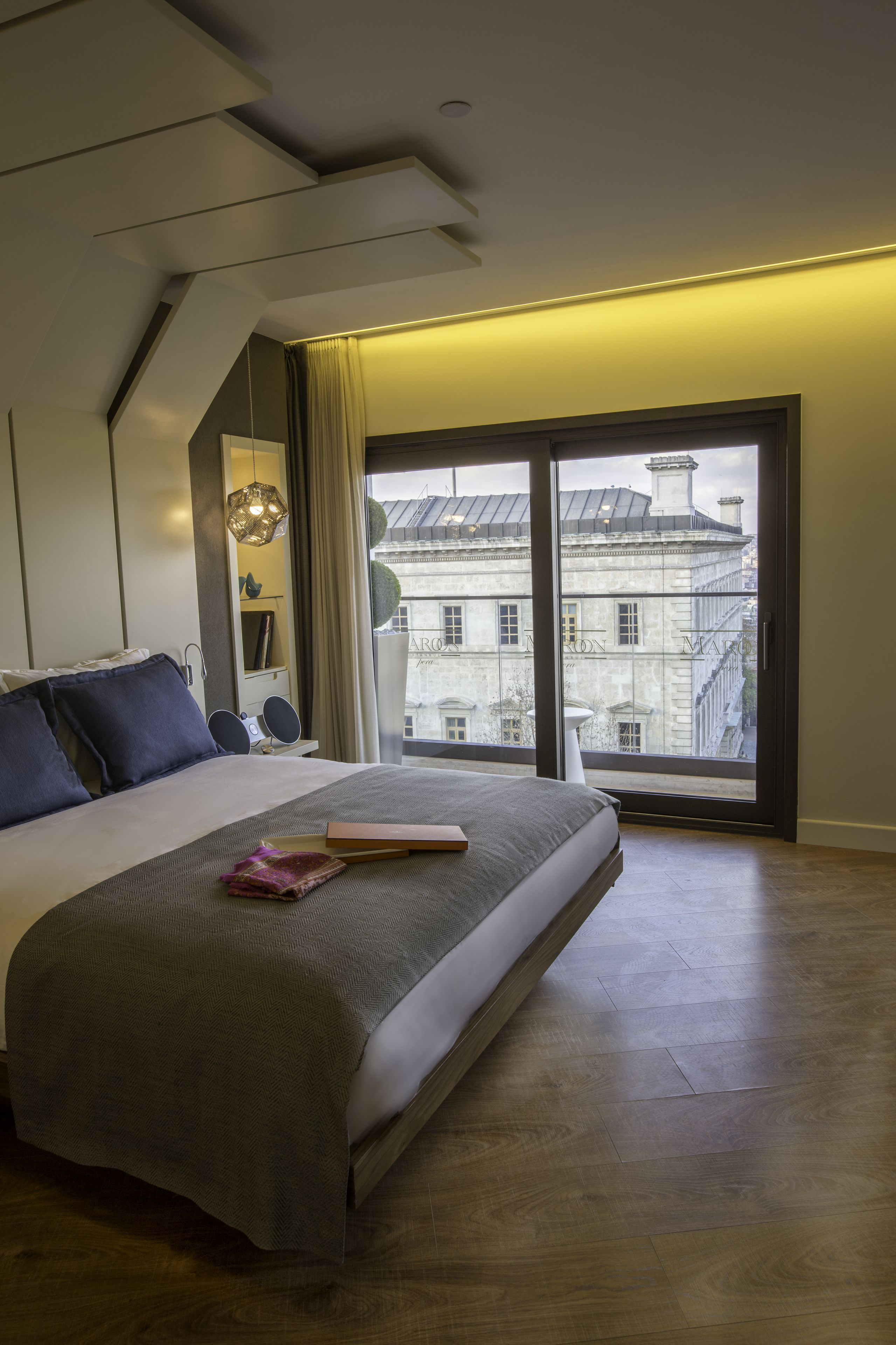 Un dormitorio moderno con una cama grande, vistas a edificios a través de una puerta corrediza y una lámpara en el techo.