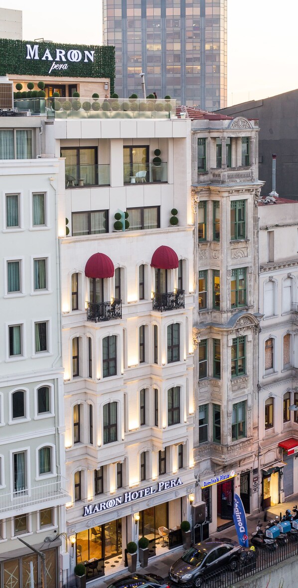 Un hôtel à plusieurs étages, de style architectural classique, doté de balcons ornés d’auvents rouges et d’une enseigne de restaurant bien visible.