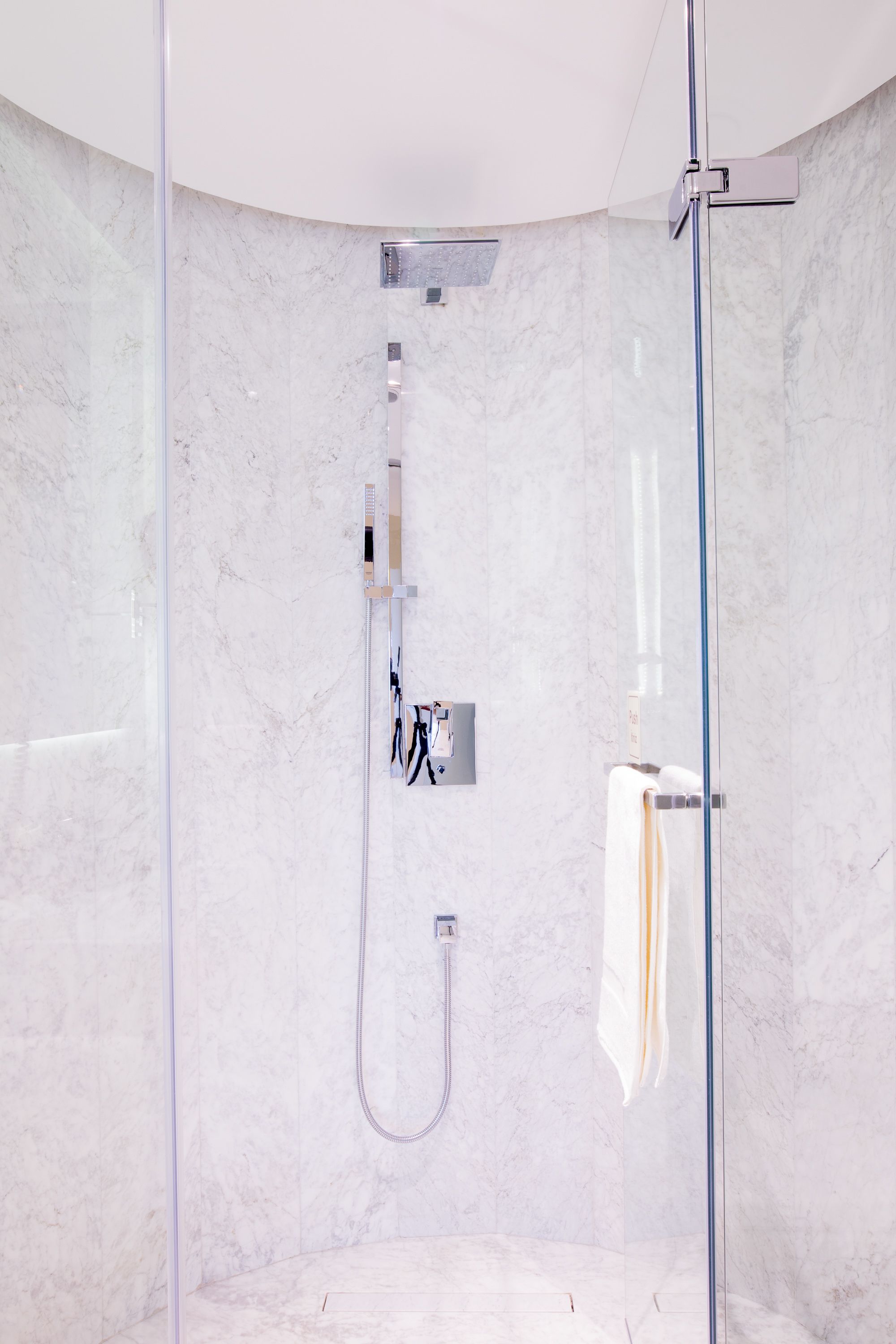 A modern bathroom with a glass-enclosed shower, marble walls, and a towel rack.