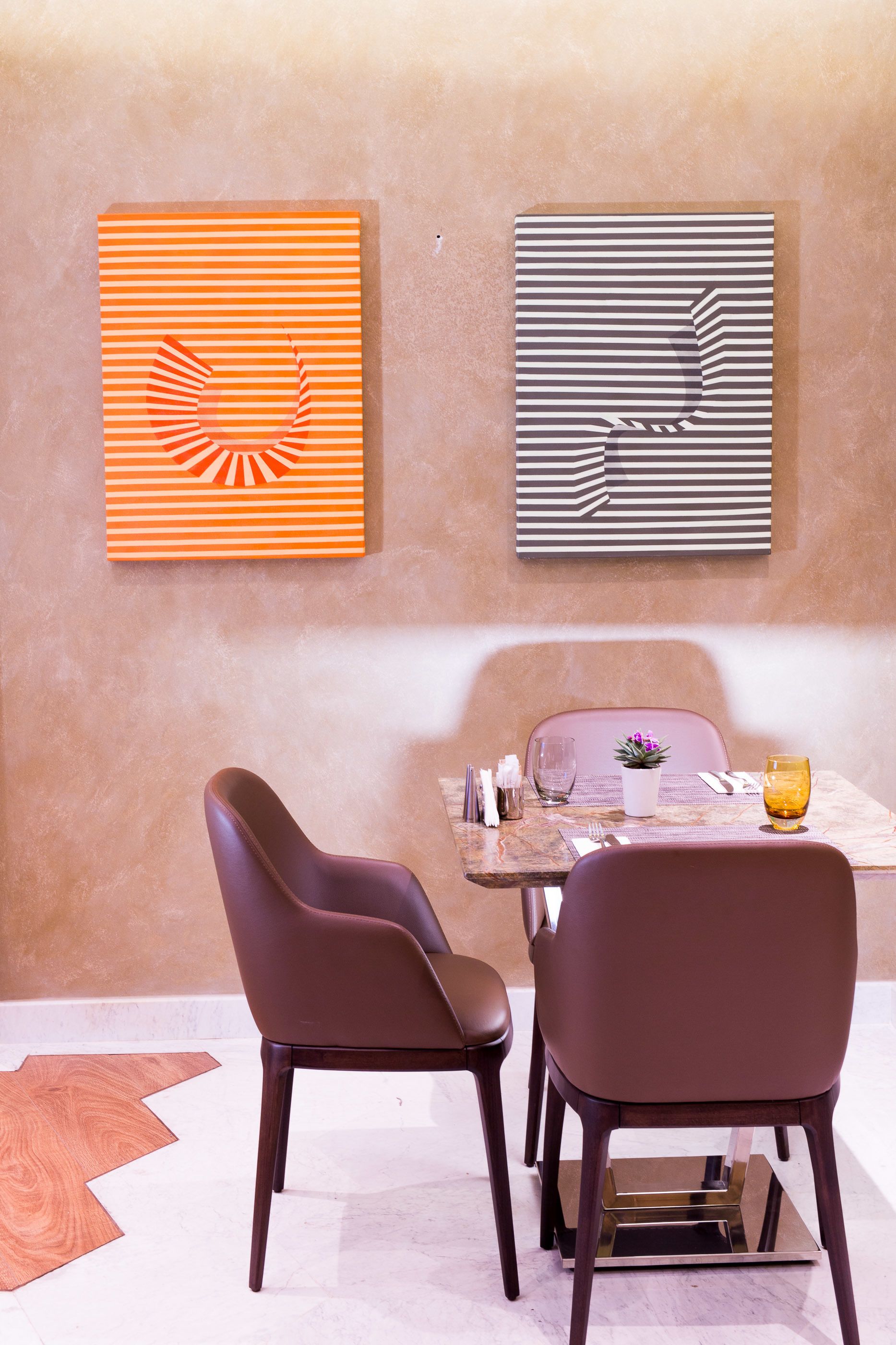 Un coin repas avec une table dressée pour deux personnes, deux chaises, une plante en pot et un verre de jus d’orange.