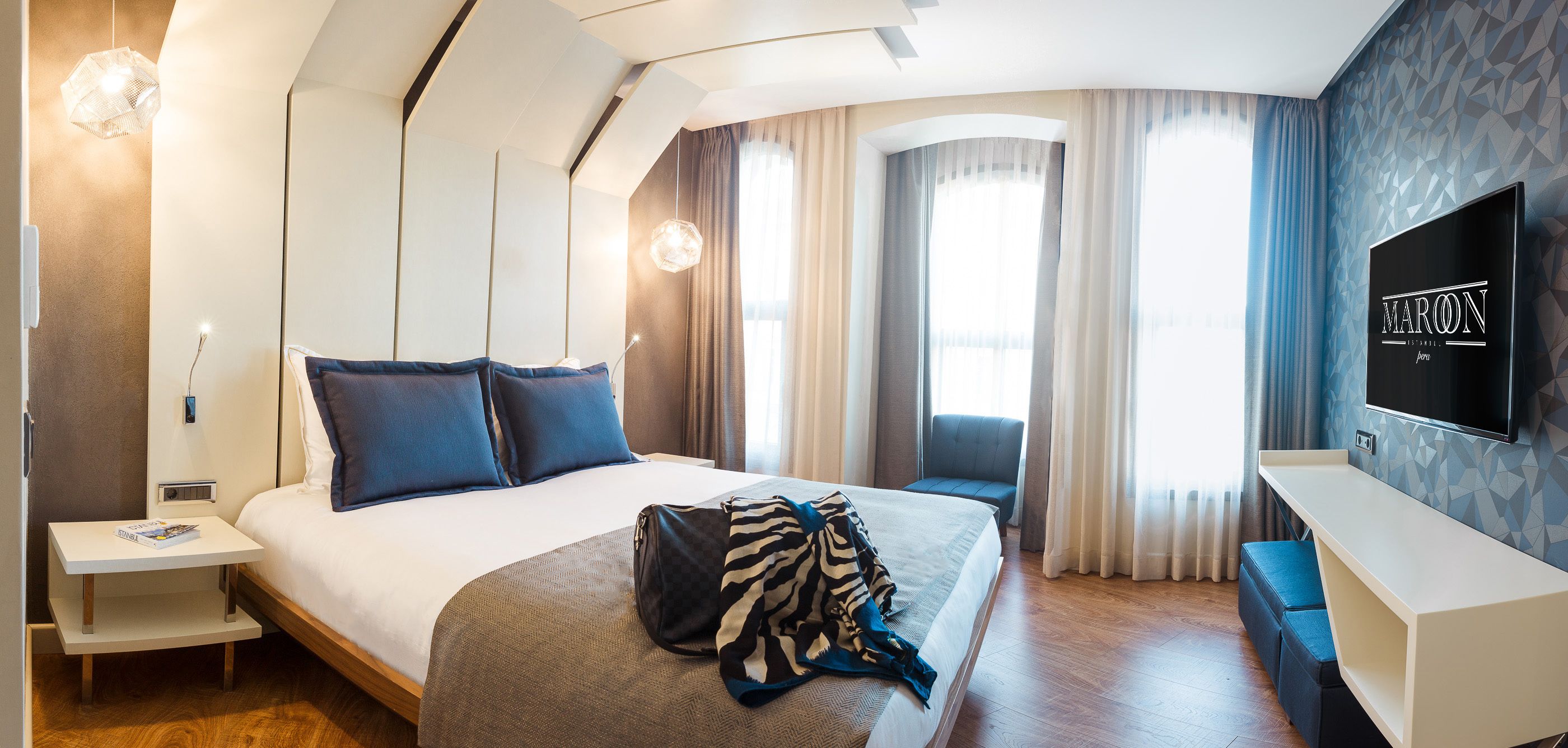 A modern hotel room with a large bed, a desk, a TV, and a seating area.
