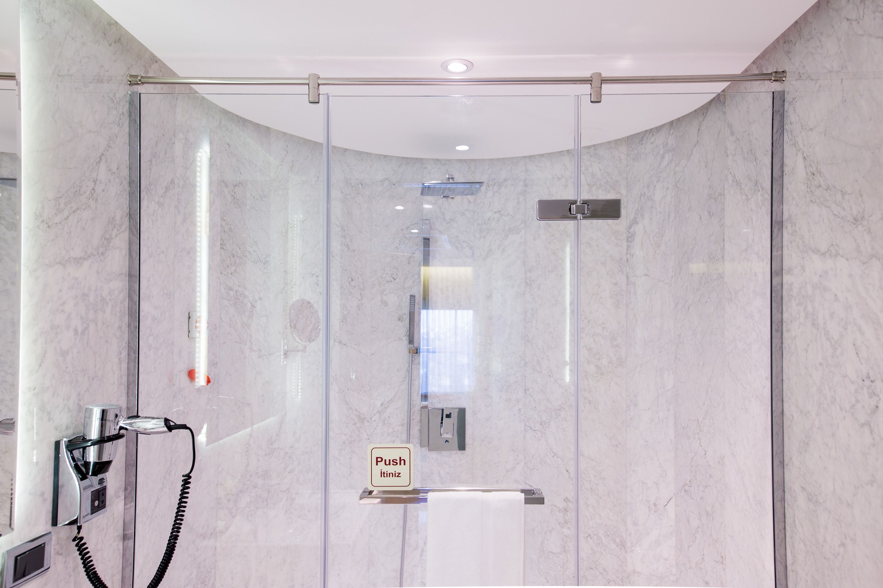 Une salle de bain moderne dotée d’une douche à parois de verre, d’un sèche-cheveux et d’un bouton-poussoir pour la douche.