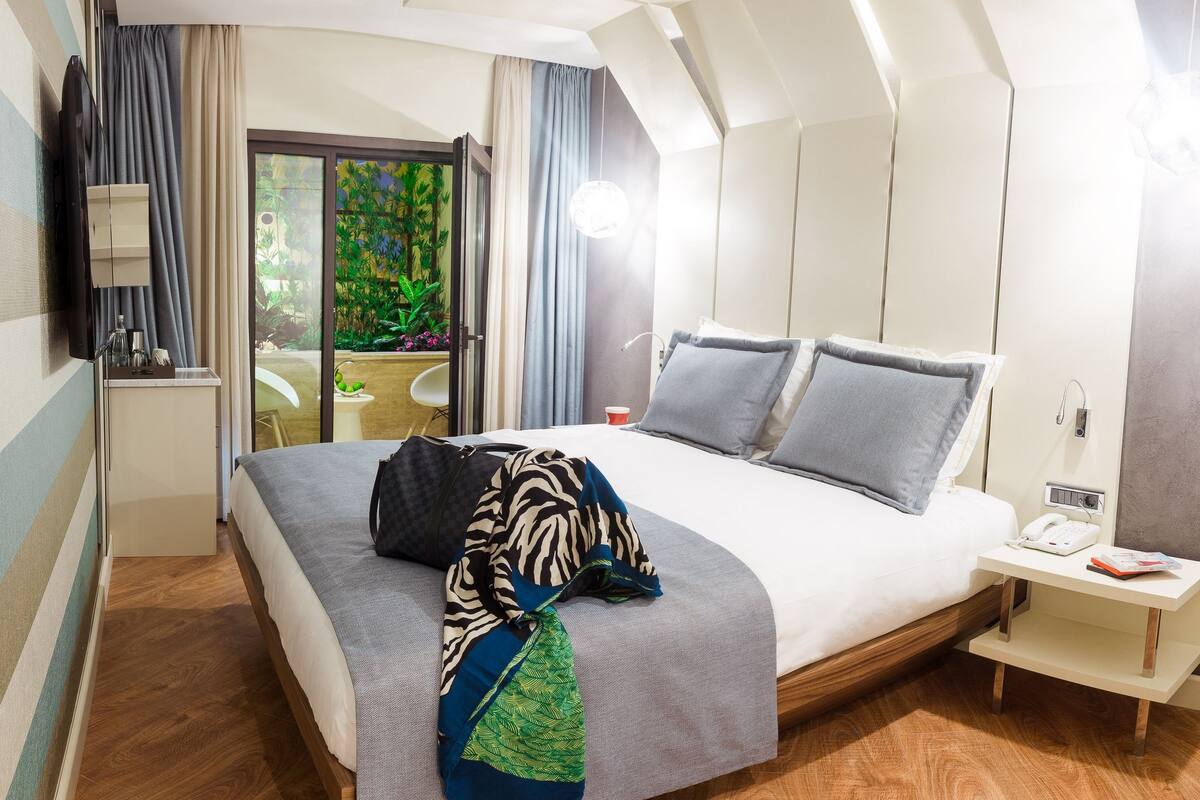 Habitación de hotel moderna con una cama grande, una mesita de noche con teléfono y vistas a un jardín por una puerta de cristal.