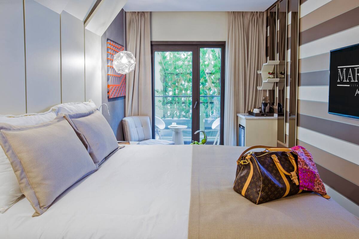 Habitación de hotel con una cama grande, vistas a zonas verdes a través de la puerta de vidrio, un televisor de pantalla plana y un minibar.