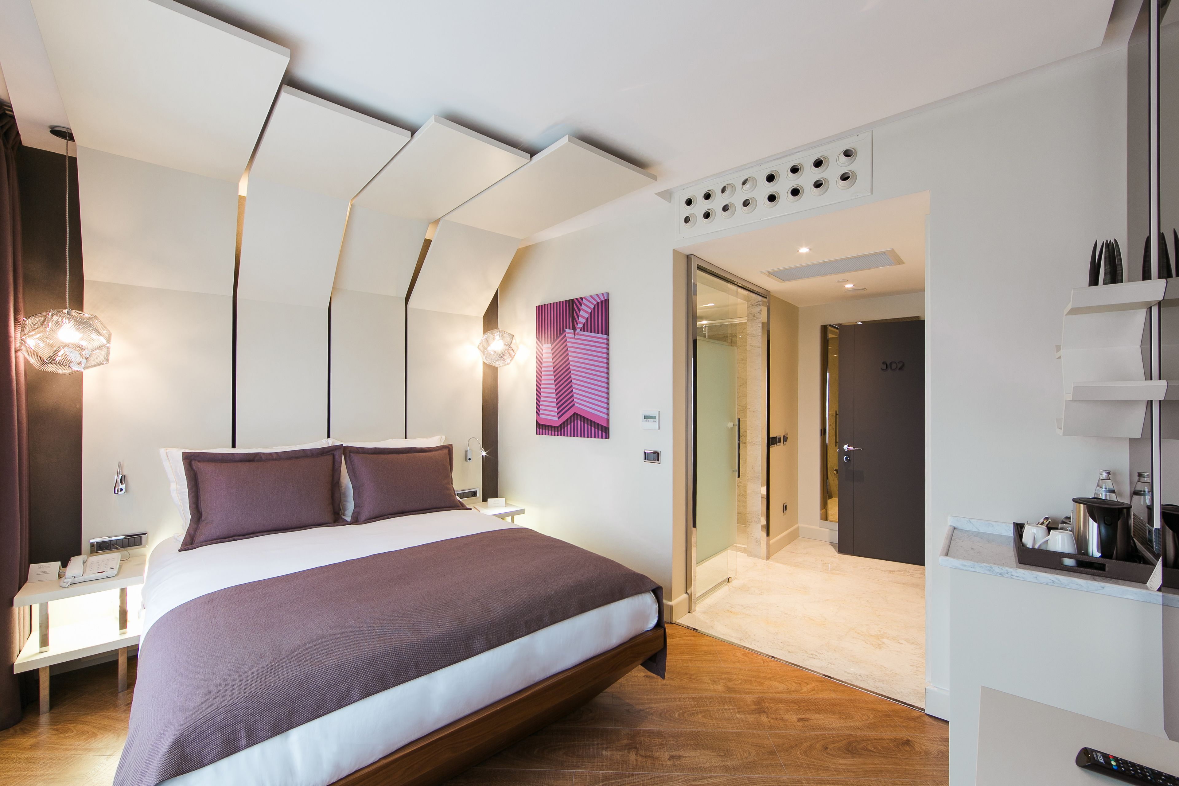 Une chambre d’hôtel moderne dotée d’un grand lit, de tables de chevet, d’un bureau et d’une salle de bain avec une douche à parois de verre.