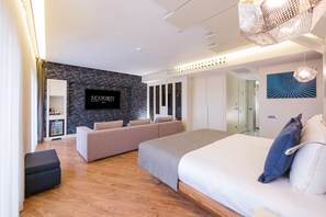 Une chambre d’hôtel moderne dotée d’un grand lit, d’un canapé, d’un téléviseur fixé au mur et d’un plancher en bois.