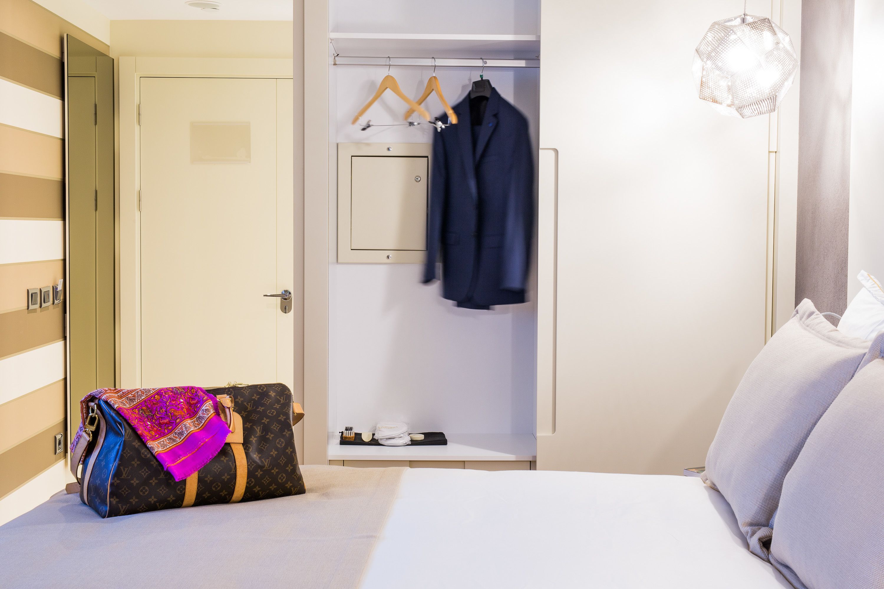 Habitación de hotel con cama, perchero, maleta y armario.