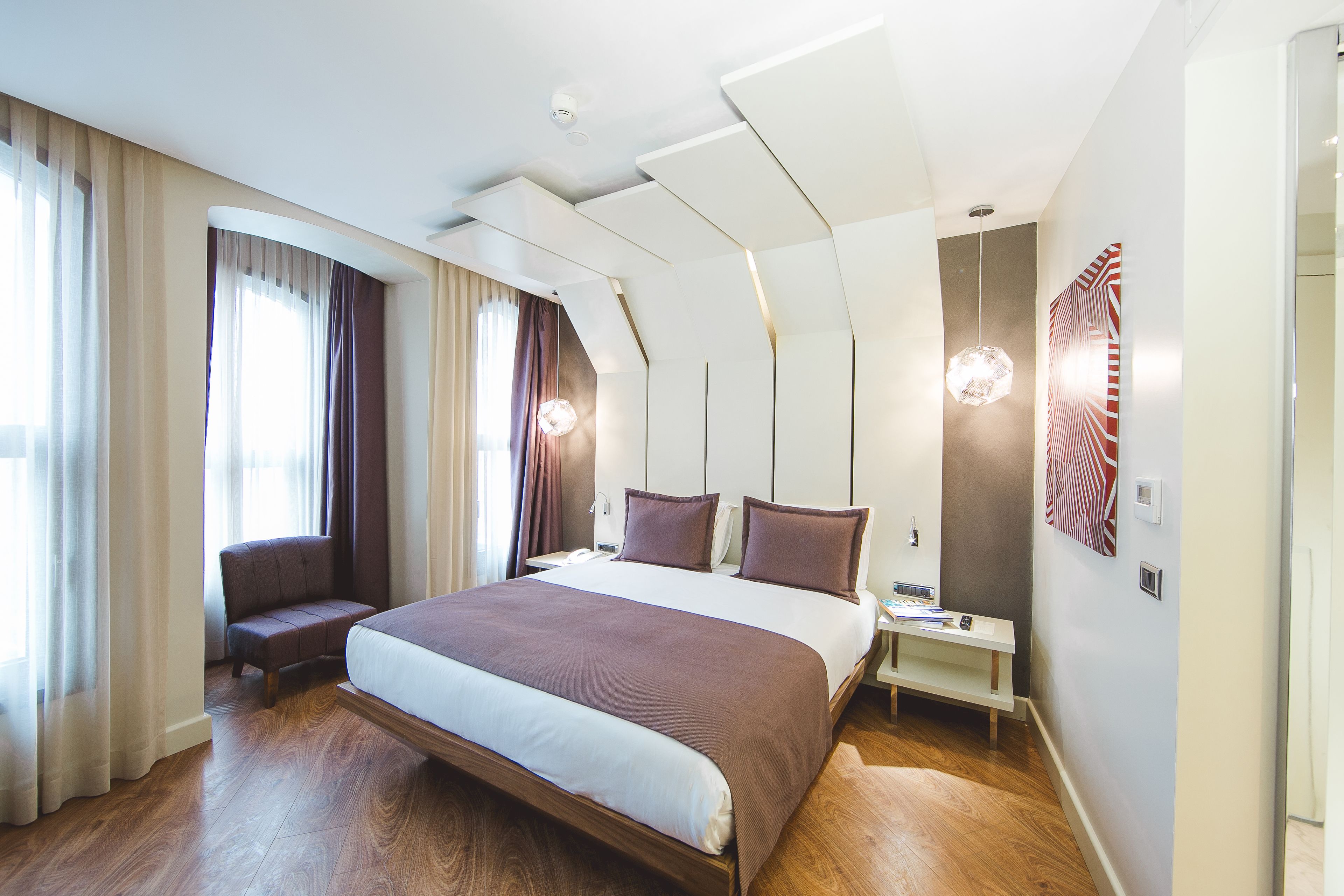 Moderni hotellihuone, jossa on suuri sänky, yöpöytä, tuoli ja työpöytä.