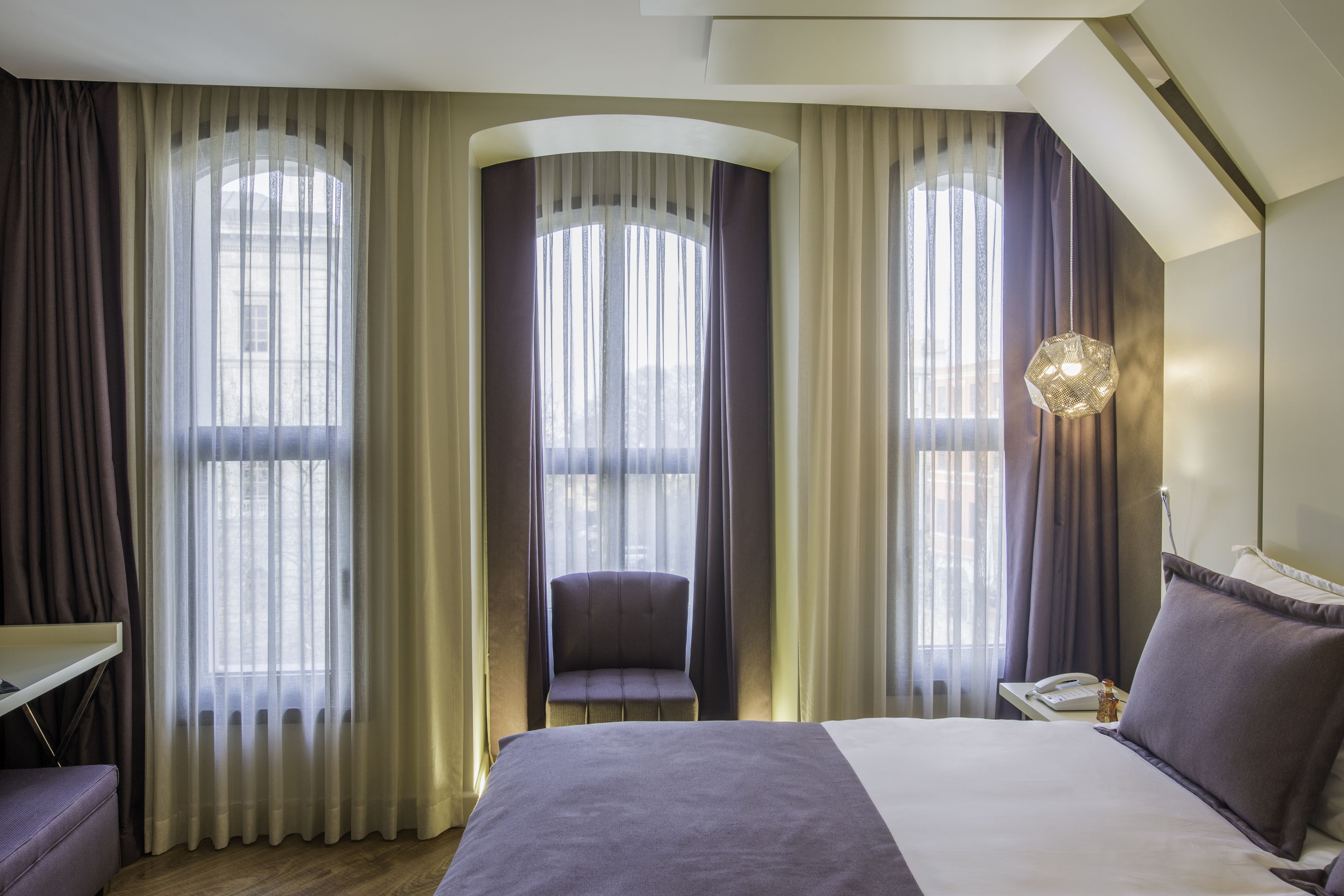 A hotel room with a large bed, a chair, a desk, and a phone on a nightstand.