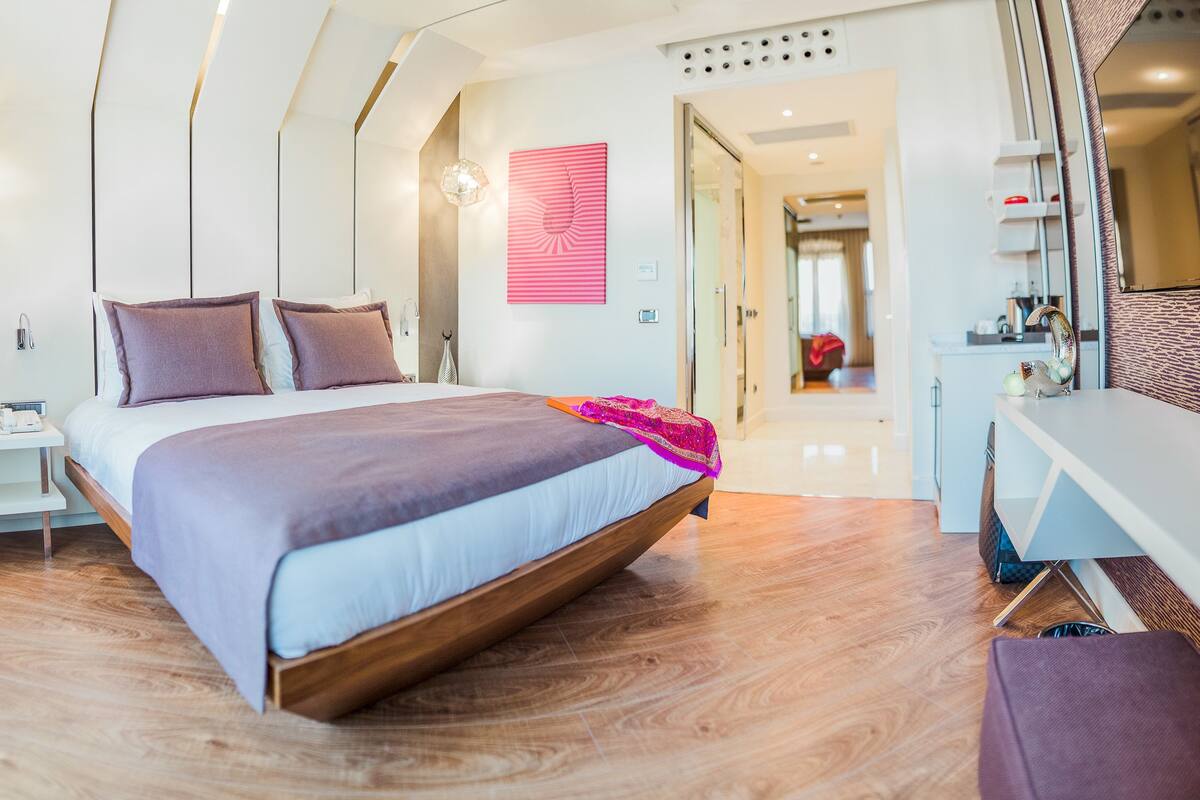 Un dormitorio moderno con una cama de madera, una mesita de noche, un espejo y una decoración rosa en la pared.