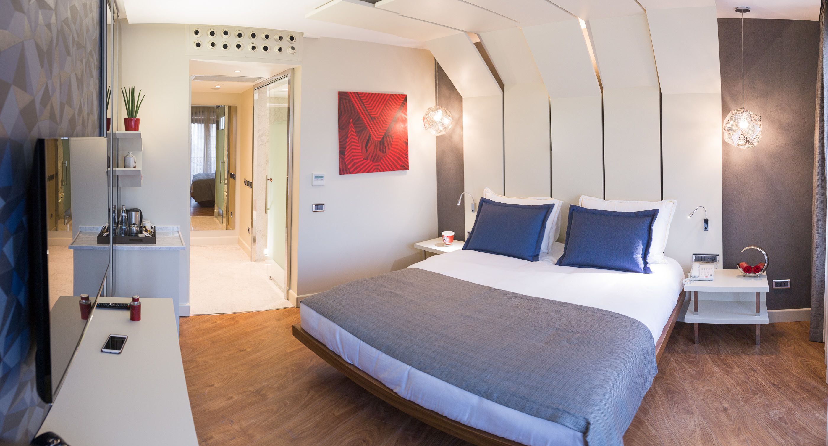 A modern hotel room with a large bed, bedside tables, a desk, and a mirror.