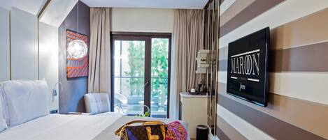 A hotel room with a bed, a large window, a TV, and a Louis Vuitton bag on the bed.